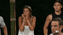 a woman in a white tank top is standing in front of a group of men .