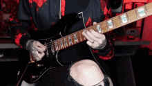a man in a red and black hoodie is playing an electric guitar .
