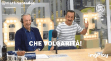 two men are sitting in front of a microphone and one of them is wearing headphones and says che volgarita