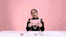 a woman is sitting at a table holding a pink box that says delish .