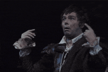 a man in a black coat is making a funny face with his hands in the air