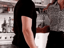 a man and a woman are standing in a kitchen and talking to each other .
