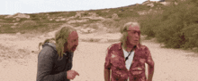 two men standing on a sandy beach talking