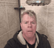 a man taking a selfie in a bathroom with a shower head above him