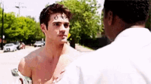 a shirtless man talking to another shirtless man on a street
