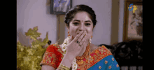 a woman in a blue and red saree is covering her mouth with her hands .