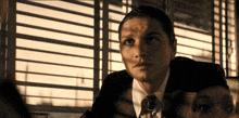 a man in a suit and tie looks out a window with blinds