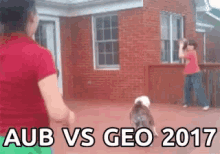 a woman in a red shirt is standing next to a dog in front of a brick building with the words aub vs geo 2017 above her