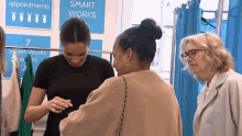 a woman is talking to another woman in front of a sign that says " smart works "