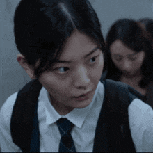 a girl in a white shirt and blue tie looks at the camera