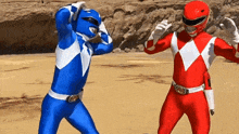 a blue power ranger and a red power ranger are standing next to each other on a sandy beach .