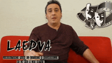 a man sits on a red couch in front of a sign that says laedva on it