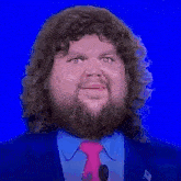 a man with curly hair and a beard is wearing a pink tie and a blue suit .