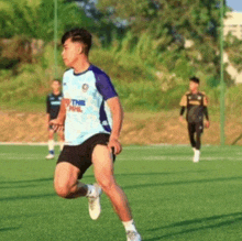 a man in a blue shirt and black shorts is running on a soccer field with other players .