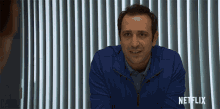 a man in a blue jacket is sitting in front of a netflix logo