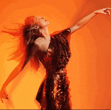 a woman in a red dress is dancing in front of an orange background