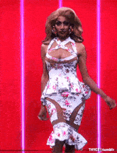 a drag queen is walking down the runway wearing a floral dress and earrings .