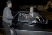 a man is standing next to a woman in a car and talking to her .