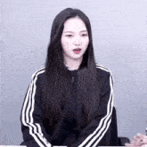 a girl with long black hair is wearing a black jacket with white stripes