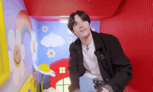 a young man in a black jacket is standing in a room with a rainbow and smiley face on the wall .