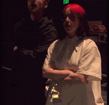 a woman in a white shirt is dancing in front of a green exit sign