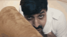 a man with a beard is hiding behind a couch and looking at the camera .