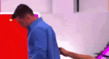 a man in a blue shirt is standing in front of a red wall and a woman is holding his arm .