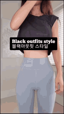a woman wearing a black crop top and blue leggings is standing in front of a window .