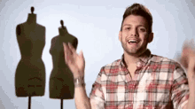 a man in a plaid shirt is standing in front of three mannequins and waving .