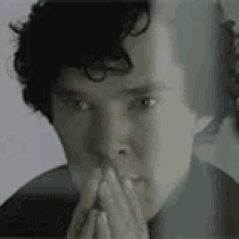 a close up of a man 's face with his hands to his mouth .