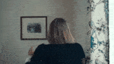 a woman is standing in front of a window with a picture on the wall behind her
