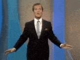 a man in a suit and tie is standing with his arms outstretched in front of a blue wall .