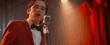 a young man in a red suit and bow tie is singing into a microphone on a stage .