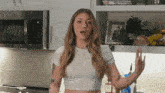 a woman in a white crop top stands in front of a microwave and a picture of a man