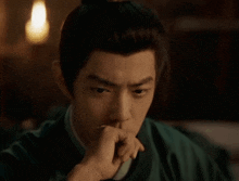 a man in a green robe is holding his hand to his mouth .