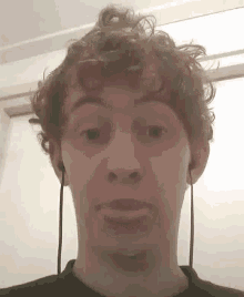 a man with curly hair is wearing headphones and making a face .