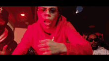 a man in a red hoodie is standing in a kitchen under red lights