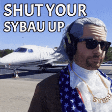 a man wearing a wig and sunglasses stands in front of a plane with the words shut your sybau up above him