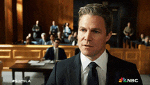 a man in a suit and tie is standing in front of a nbc sign