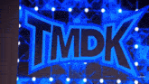 a wrestler stands in front of a large tmpk logo