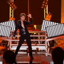 a man in a black leather jacket is dancing on stage
