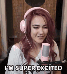 a woman wearing pink headphones is sitting in front of a microphone and saying `` i 'm super excited `` .