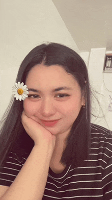 a woman wearing a striped shirt and a flower in her hair is smiling .