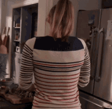 a woman in a striped shirt is standing in front of a fridge