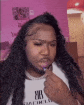 a woman with long hair and a beard is wearing a white shirt with the letter b on it .