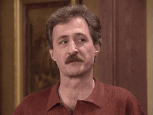a man with a mustache is waving his hand in front of a painting