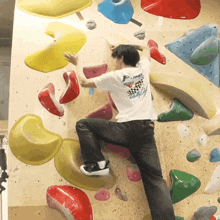 a man on a climbing wall wearing a shirt that says plum
