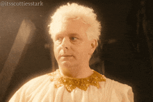 a man with white hair is wearing a gold collar and a white shirt