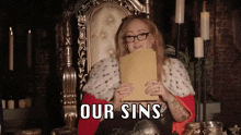 a woman sitting in a chair holding a piece of paper that says " our sins "