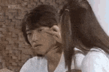 a woman is touching a man 's face while sitting next to him .